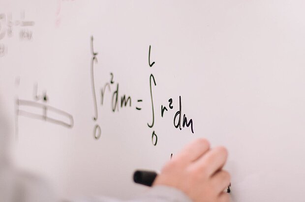 Hände große, welche eine mathematische Formel an ein Whiteboard schreiben.